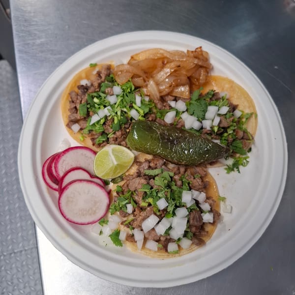 Plate of tacos topped with grilled meat, onions, cilantro, and roasted jalapeño, served with lime and radish slices.