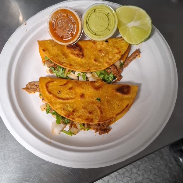 Two birria tacos with cilantro and onions, served with red and green salsa, and lime wedges.